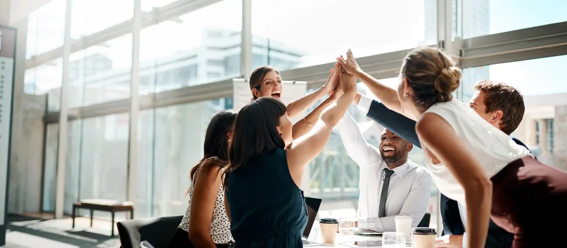 Shot of a group of businesspeople high fiving while sitting in a meeting